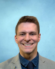 Photograph of Jake standing in front of a blue background.