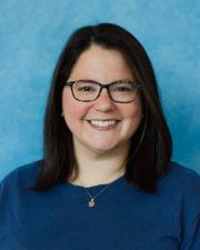 Photograph of Rosana standing in front of a blue background.